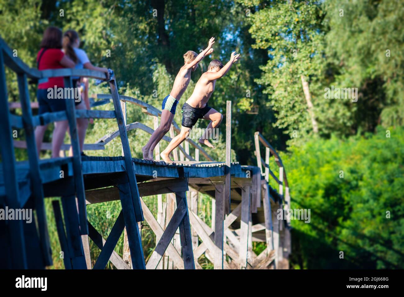 Children jump from a wooden bridge into the river Stock Photo