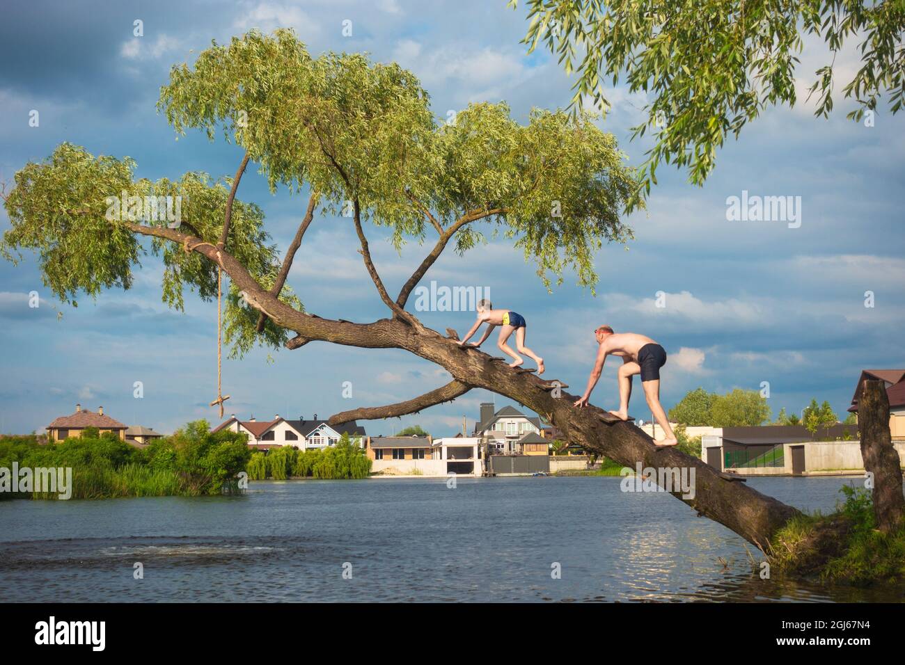 A child and an adult climb a tree trunk above the water. Jumping into