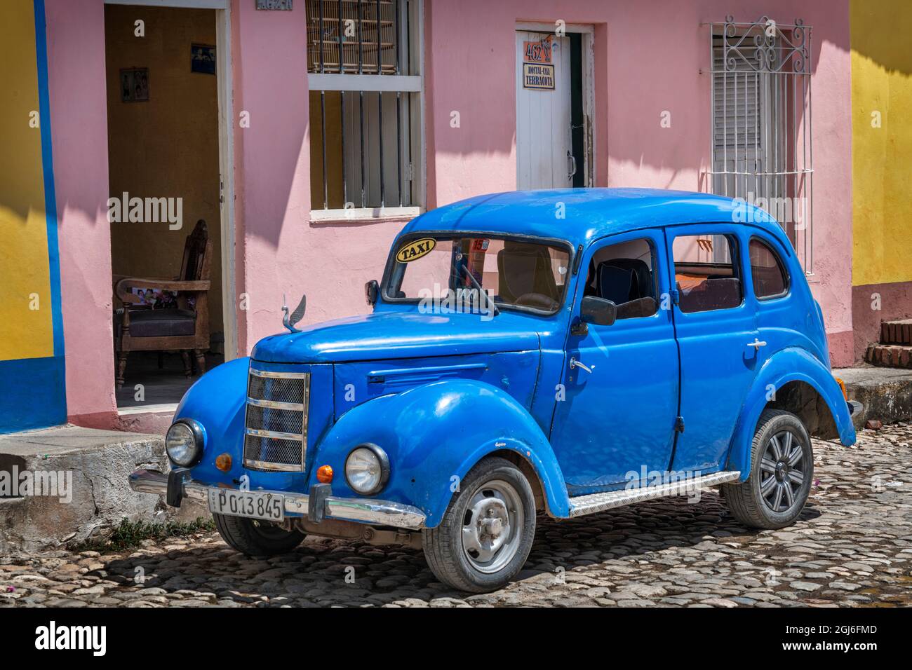 Old blue car with swan hood ornament in front of pink and yellow