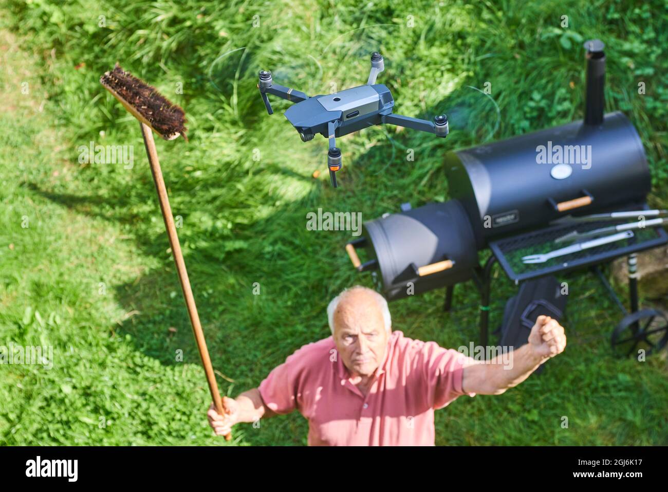 Název: Old senior man upset by a flying drone over his garden. The concept of spying on neighbors and their privacy. Man trying to knock down a drone Stock Photo