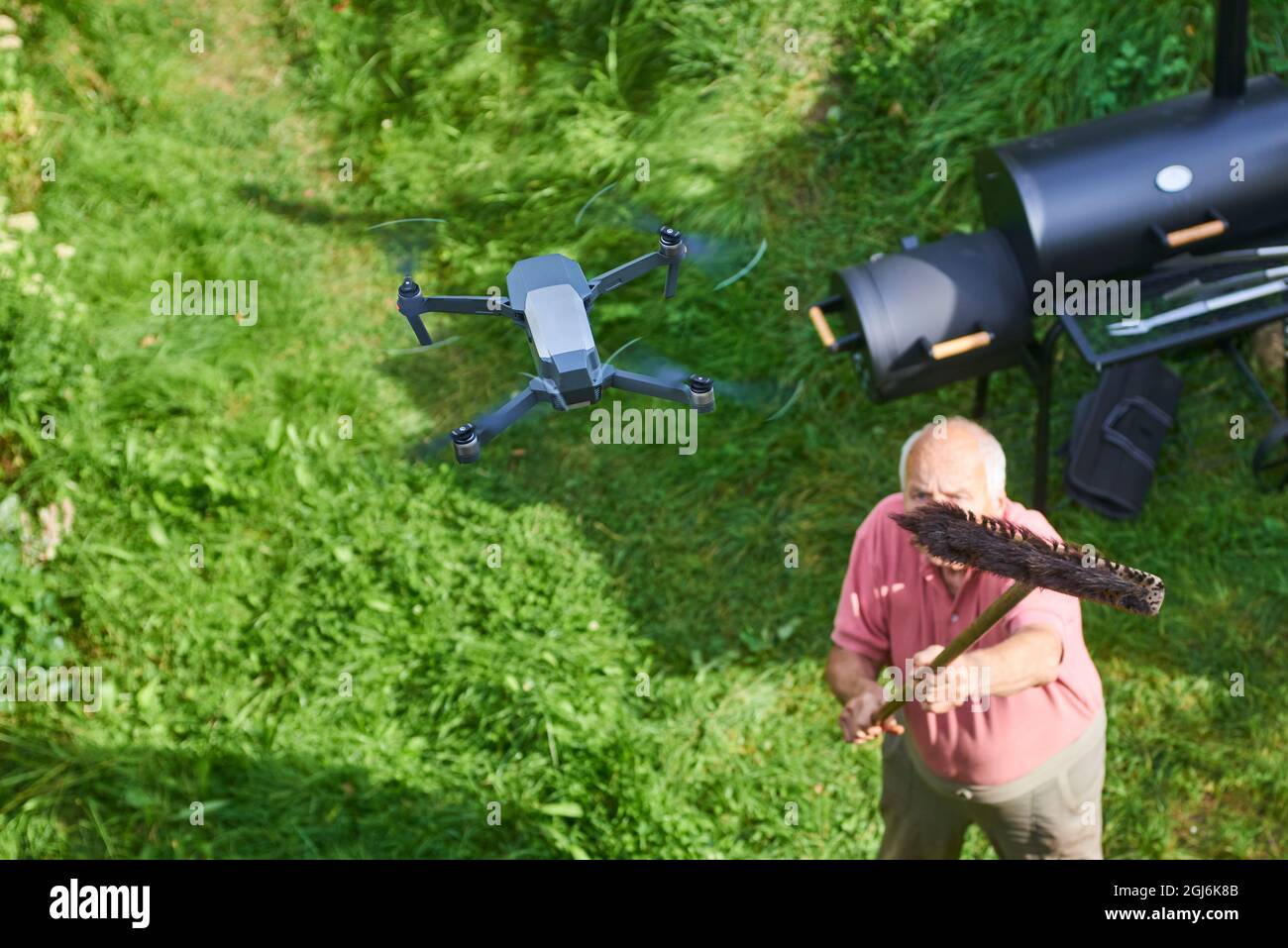 Název: Old senior man upset by a flying drone over his garden. The concept of spying on neighbors and their privacy. Man trying to knock down a drone Stock Photo