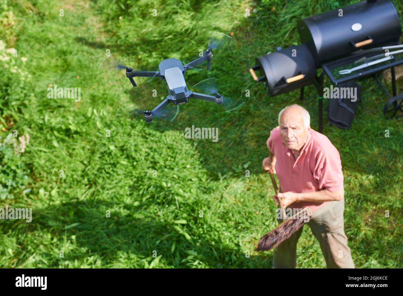 Název: Old senior man upset by a flying drone over his garden. The concept of spying on neighbors and their privacy. Man trying to knock down a drone Stock Photo
