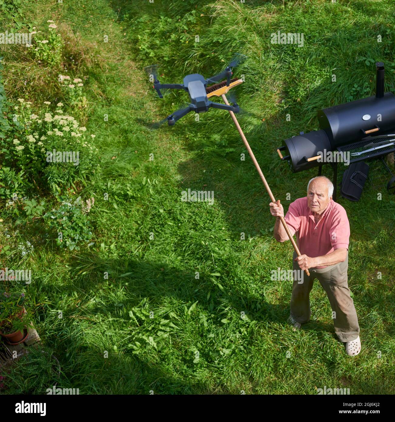 Název: Old senior man upset by a flying drone over his garden. The concept of spying on neighbors and their privacy. Man trying to knock down a drone Stock Photo