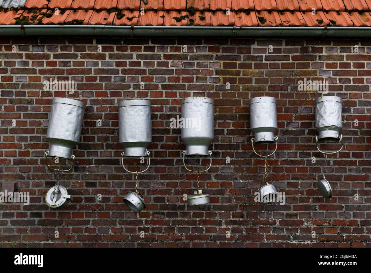 Upside-down of milk cans hanging against a brick wall Stock Photo