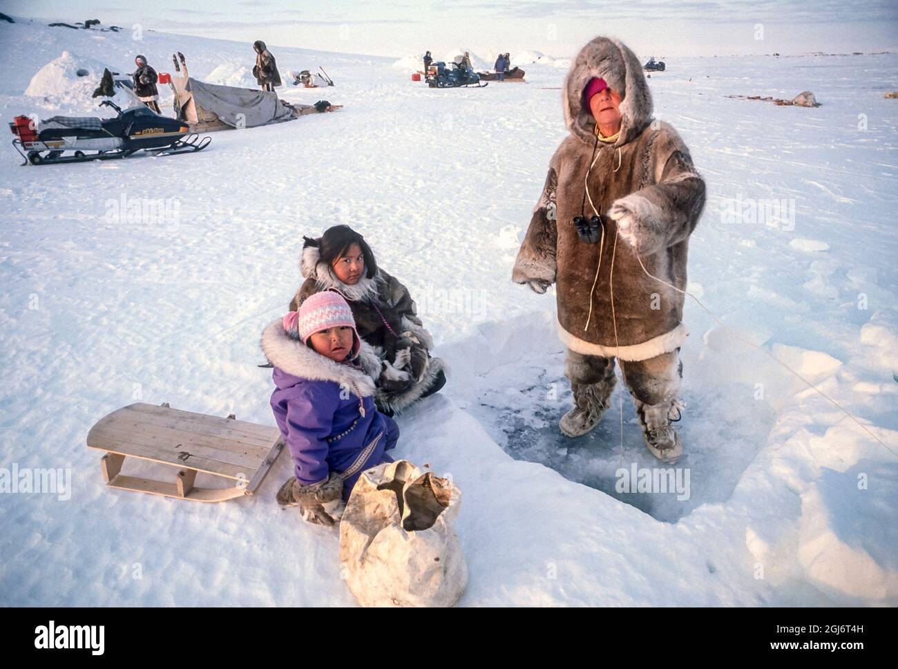 Baker Lake, Nunavut, Canada. Inuit girls, ages 4 and 11, along with woman, by fishing hole. Younger girls are dressed in traditional caribou skin clot Stock Photo