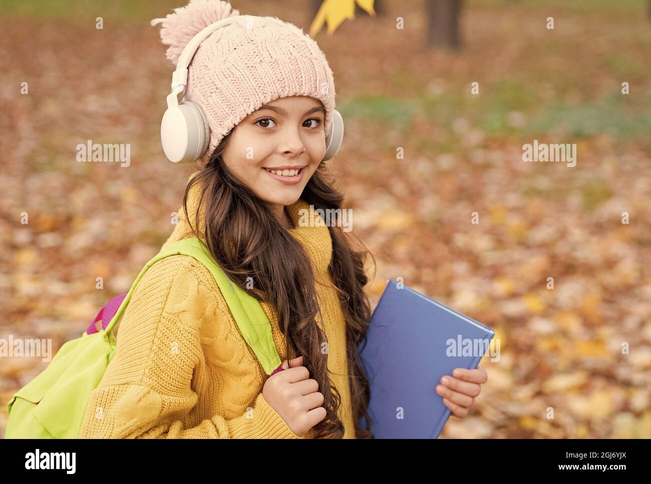 pupil in earpieces hold book while walking in park, education Stock Photo