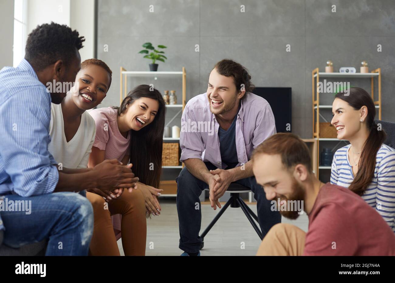 Group of happy young friends sitting in the living-room and laughing at a funny joke Stock Photo