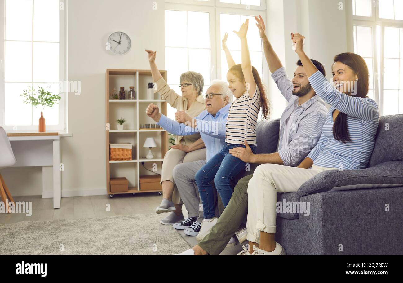 Active large family of different generations watching a football match sitting on the couch at home. Stock Photo