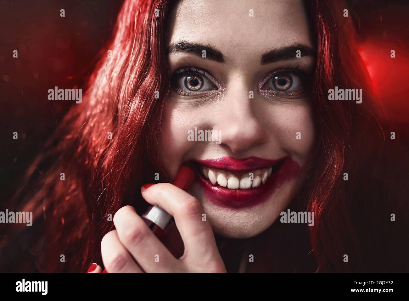 Halloween Time. Portrait of crazy-looking horror woman with red hair she is smearing red lipstick on her face, horror concept. Fear and nightmare Stock Photo