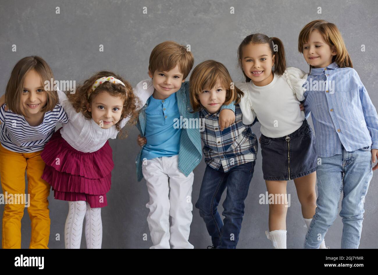 Happy children having fun standing in row hugging against grey studio copy space Stock Photo
