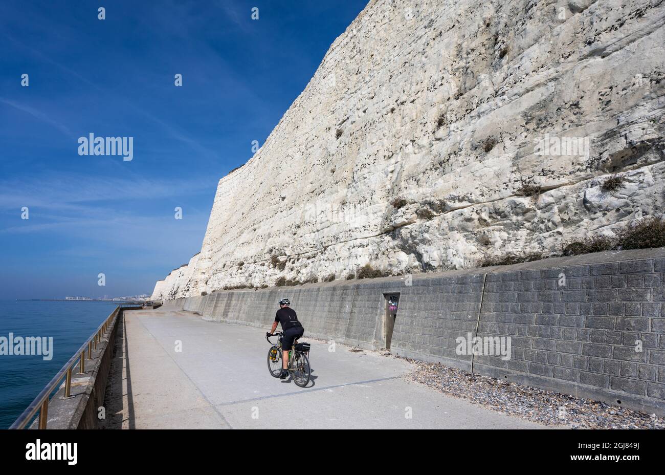 Cyclist on Rottingdean cliff path at the white chalk cliffs in Summer with blue sky in Rottingdean, on the South Coast of East Sussex, England, UK. Stock Photo