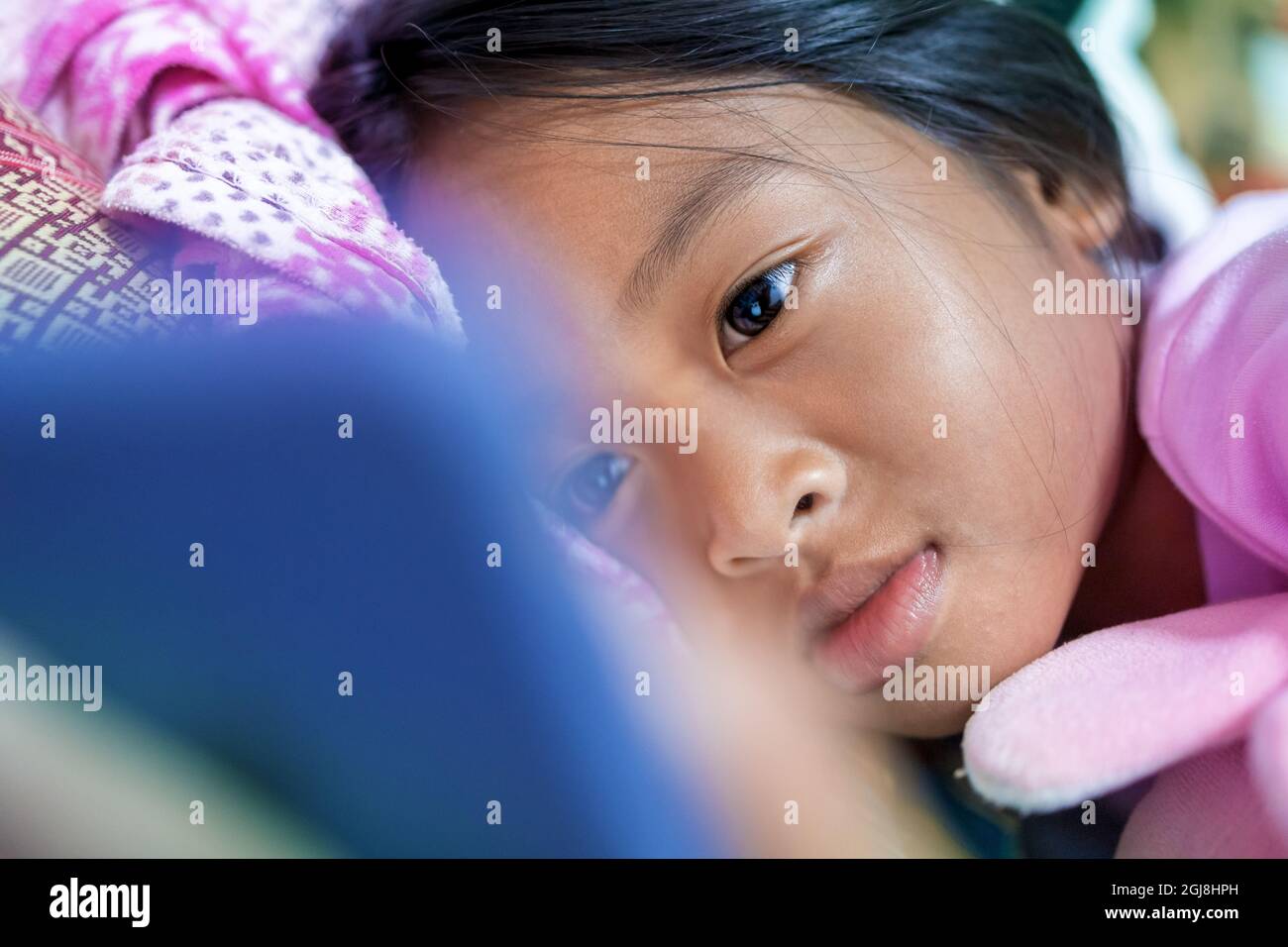 Asian girl lays happily watching cartoons on her smartphone in her bed at night. Stock Photo