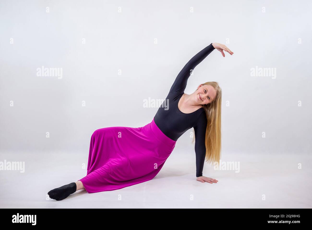 Young blonde blue-eyed dancer woman in long purple skirt on white background Stock Photo