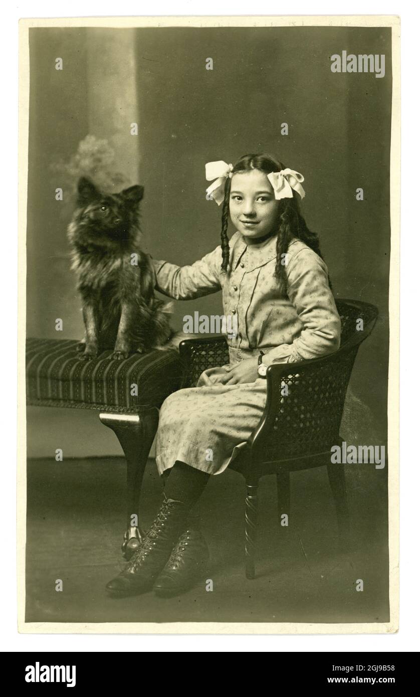 Original early 1900's, WW1 era studio portrait image of pretty smiling British Asian girl wearing loose ringlets with a pet dog. U.K. circa 1917 Stock Photo