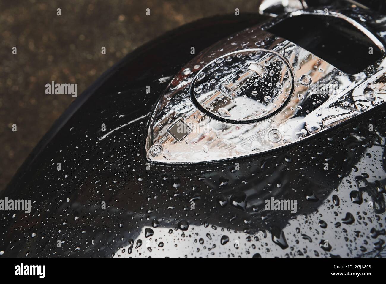 Bike covered with water drops after rain. Black gasoline tank with metal fuel cap. Outdoor vehicle storage. Closeup. Stock Photo