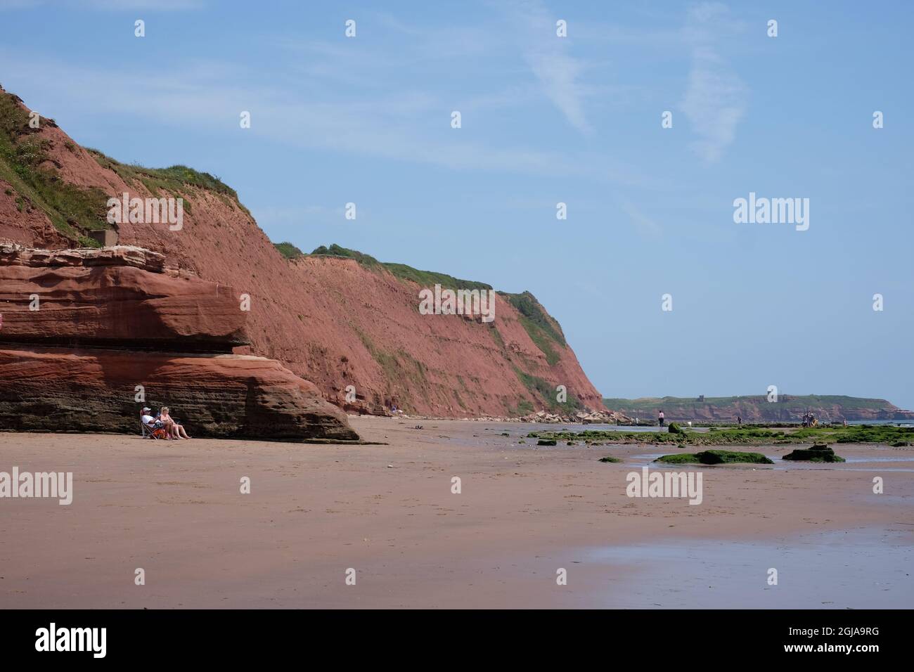 A couple relax on the beach under the red sandstone cliffs of Orcombe Point. Exmouth, Devon. Stock Photo