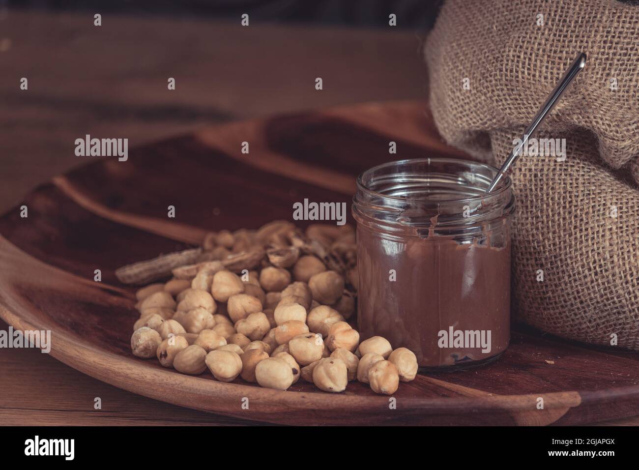 Hazelnuts and chocolate spread accompanied by gunny sack on a wooden plate Stock Photo