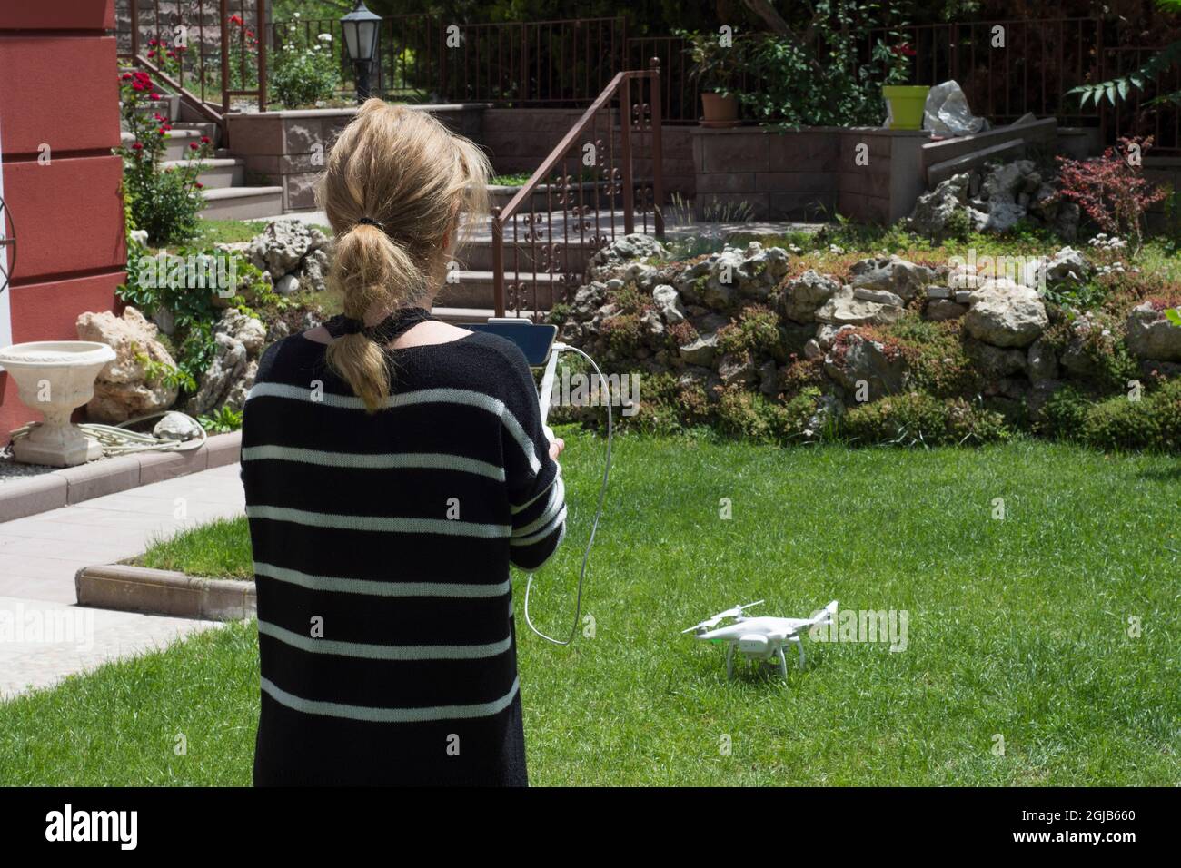 young woman flying drone in the garden of their house. Selective Focus remote control. Stock Photo