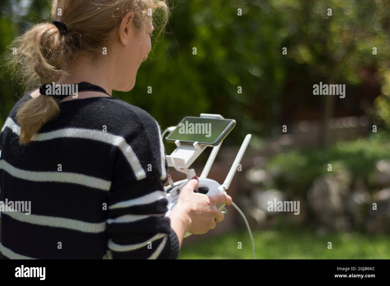 young woman flying drone in the garden of their house. Selective Focus remote control. Stock Photo