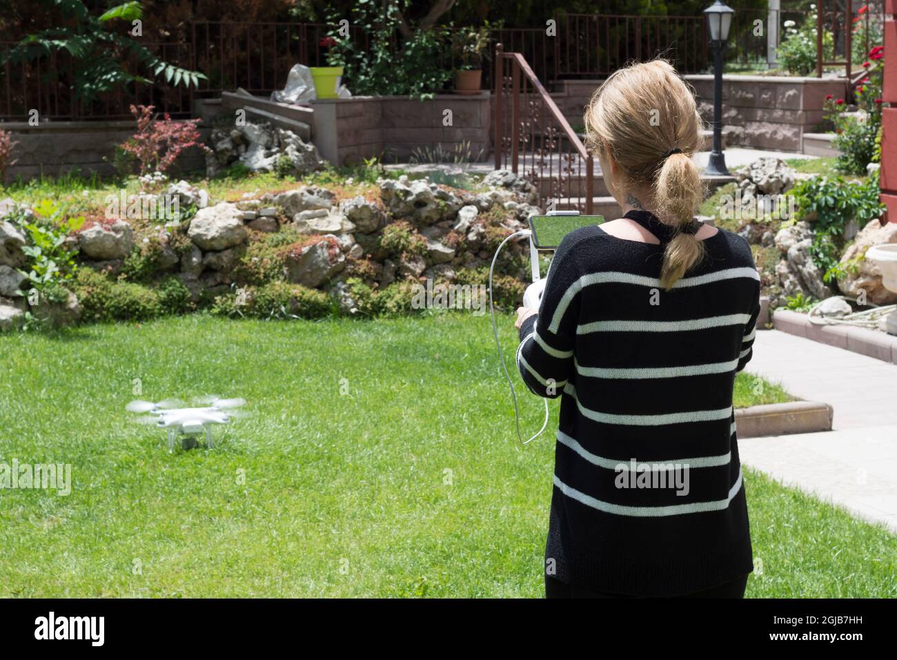 young woman flying drone in the garden of their house. Selective Focus remote control. Stock Photo