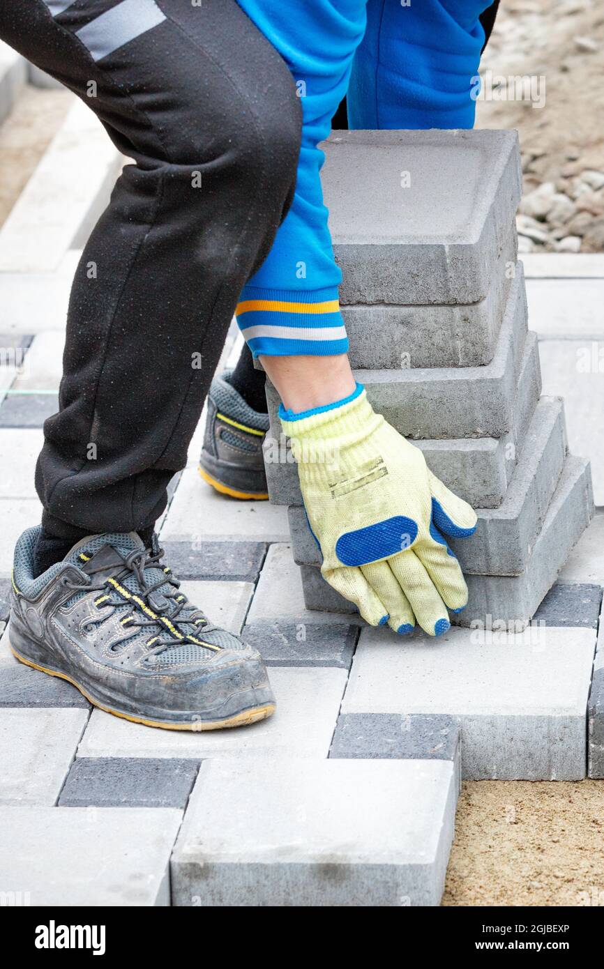 A worker wearing work gloves brings a stack of paving slabs to the work site. Vertical image. Stock Photo