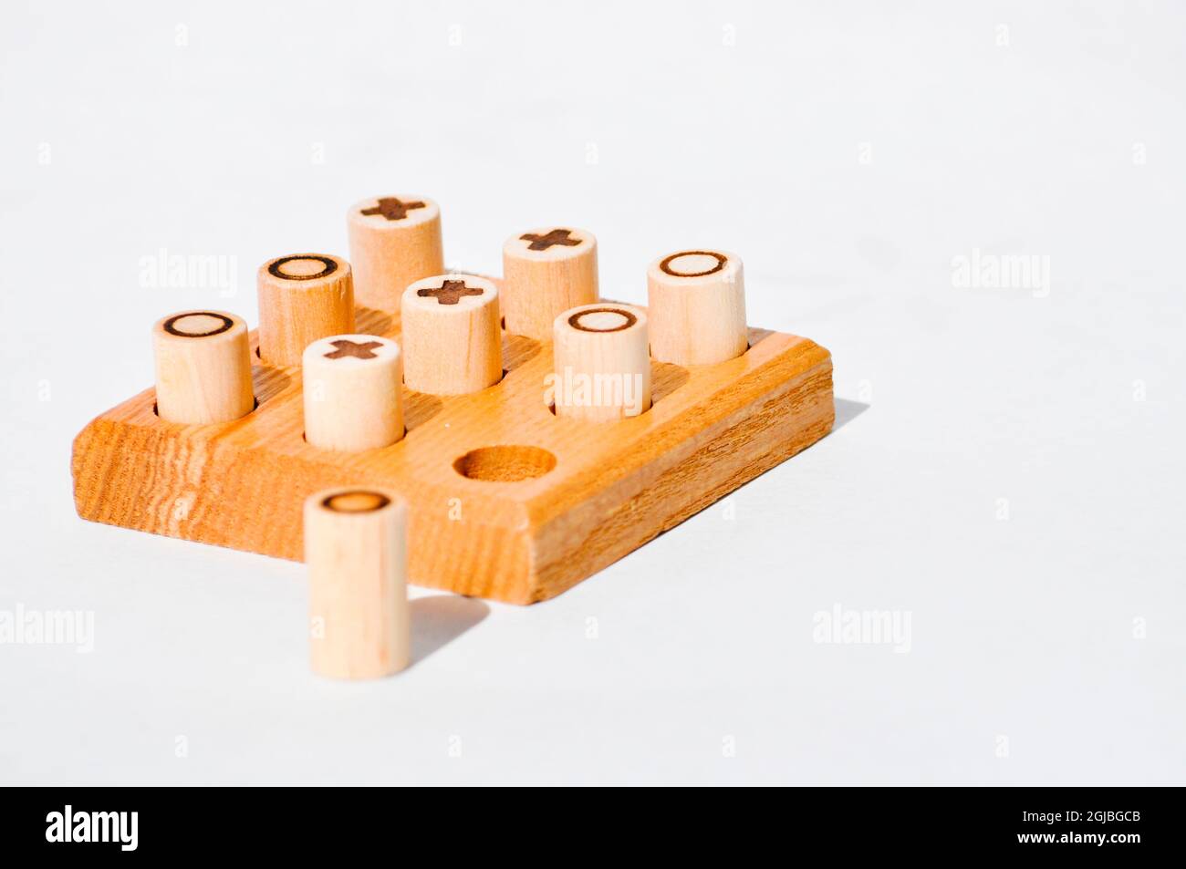 A handcrafted, wooden noughts and crosses set. Pegs are made from dowels of wood with the symbol burnt on. and the board has 9 holes drilled out. Stock Photo