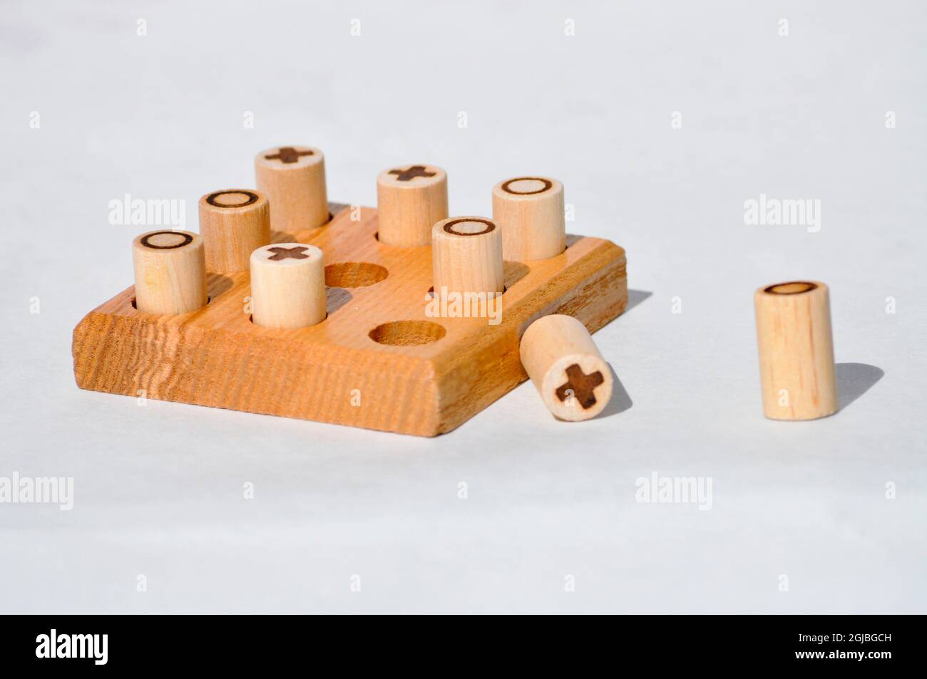 A handcrafted, wooden noughts and crosses set. Pegs are made from dowels of wood with the symbol burnt on. and the board has 9 holes drilled out. Stock Photo