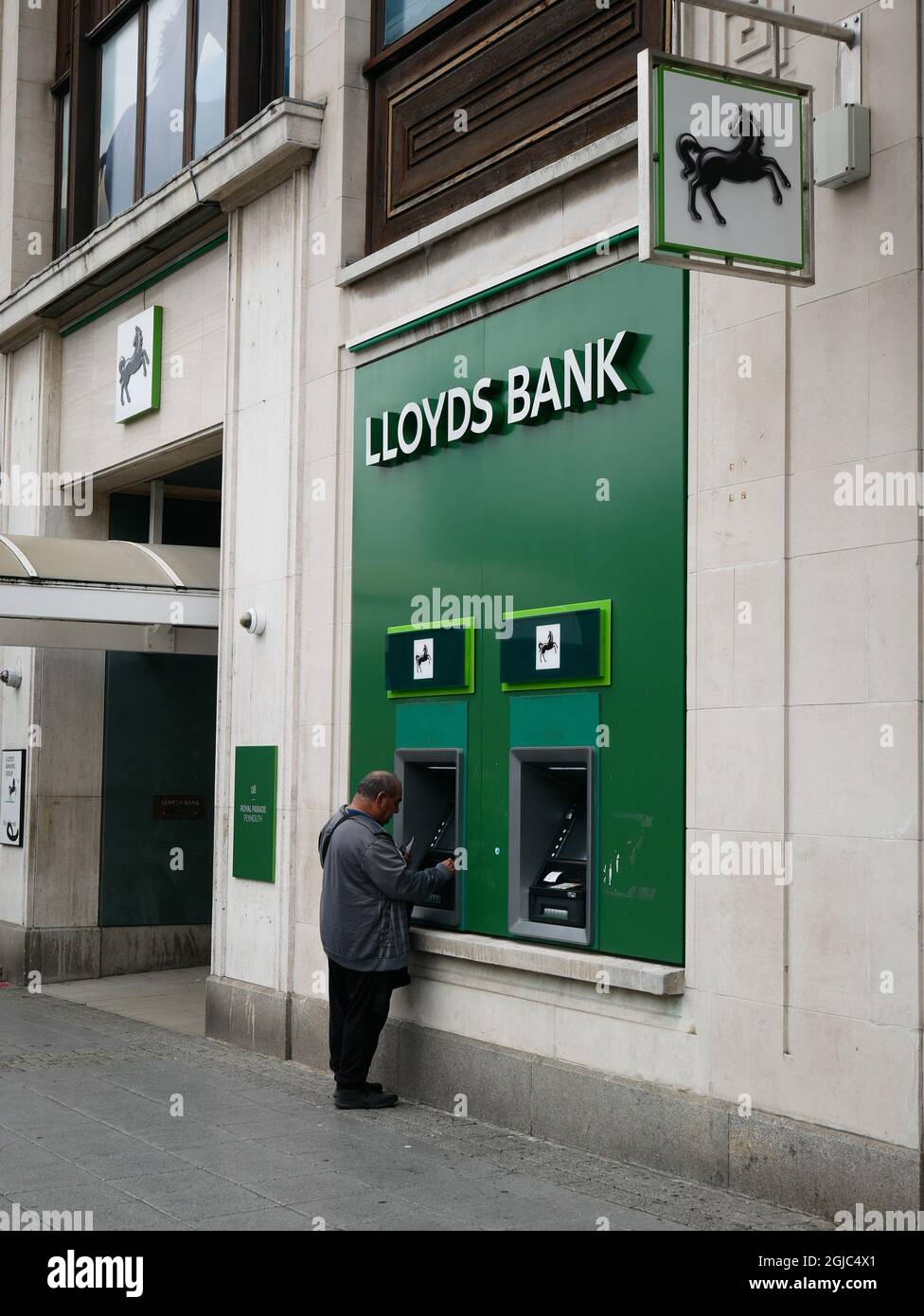 Lloyds bank high street branch with customer using exterior ATM facilities. Plymouth, UK. Stock Photo