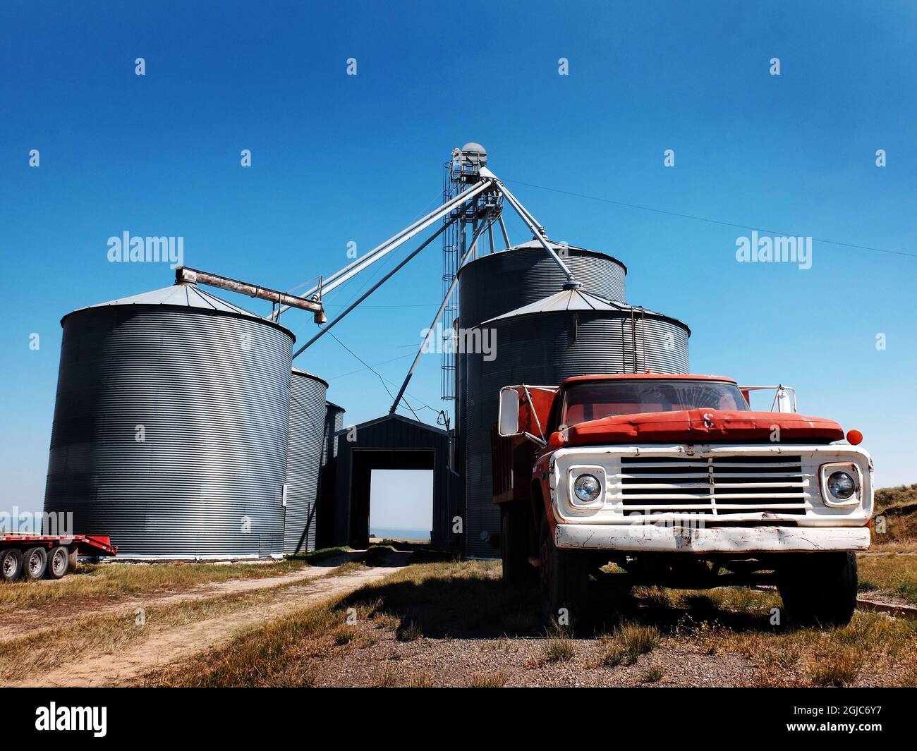 Old red work truck parked in front of several large steel grain silos ...