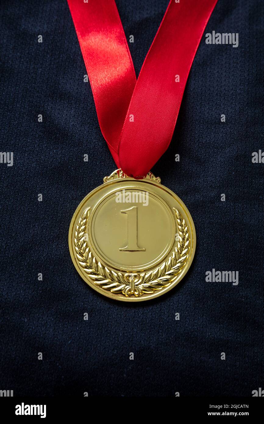 Medal gold, Winner prize award hanging with red color ribbon on athlete chest. Golden trophy in sport for first place champion on black color shirt ba Stock Photo