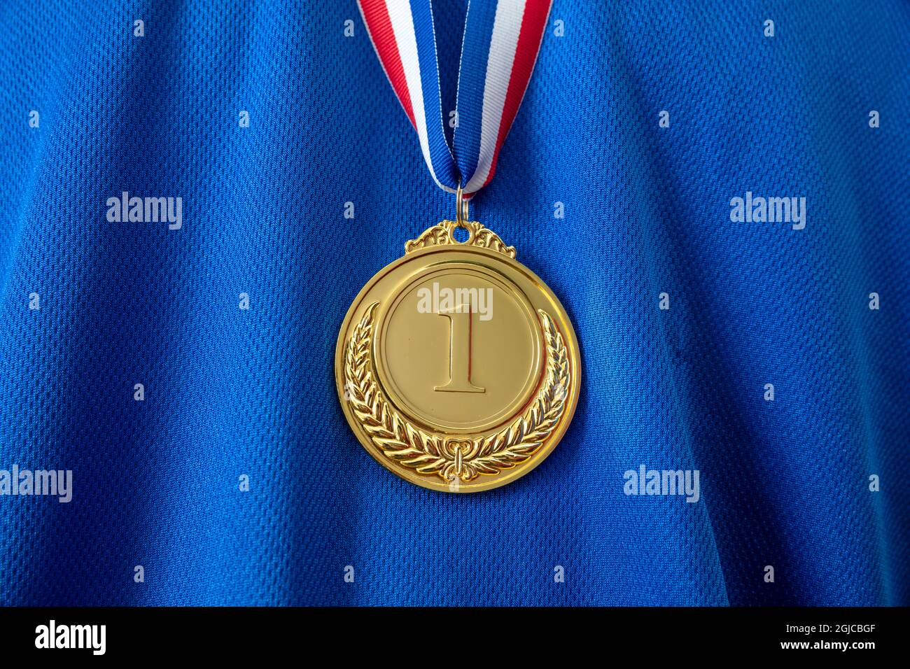 Medal gold, Winner prize award hanging with red blue color ribbon on athlete chest. Golden trophy in sport for first place champion on blue color shir Stock Photo