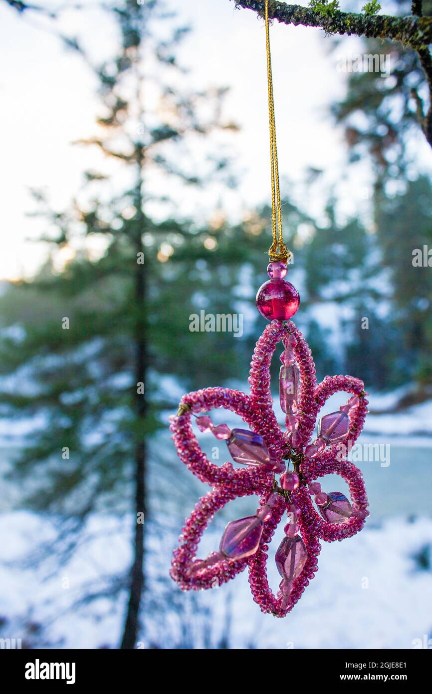 Snowflake shaped Christmas ornament hangs on a branch in a snow covered forest Stock Photo