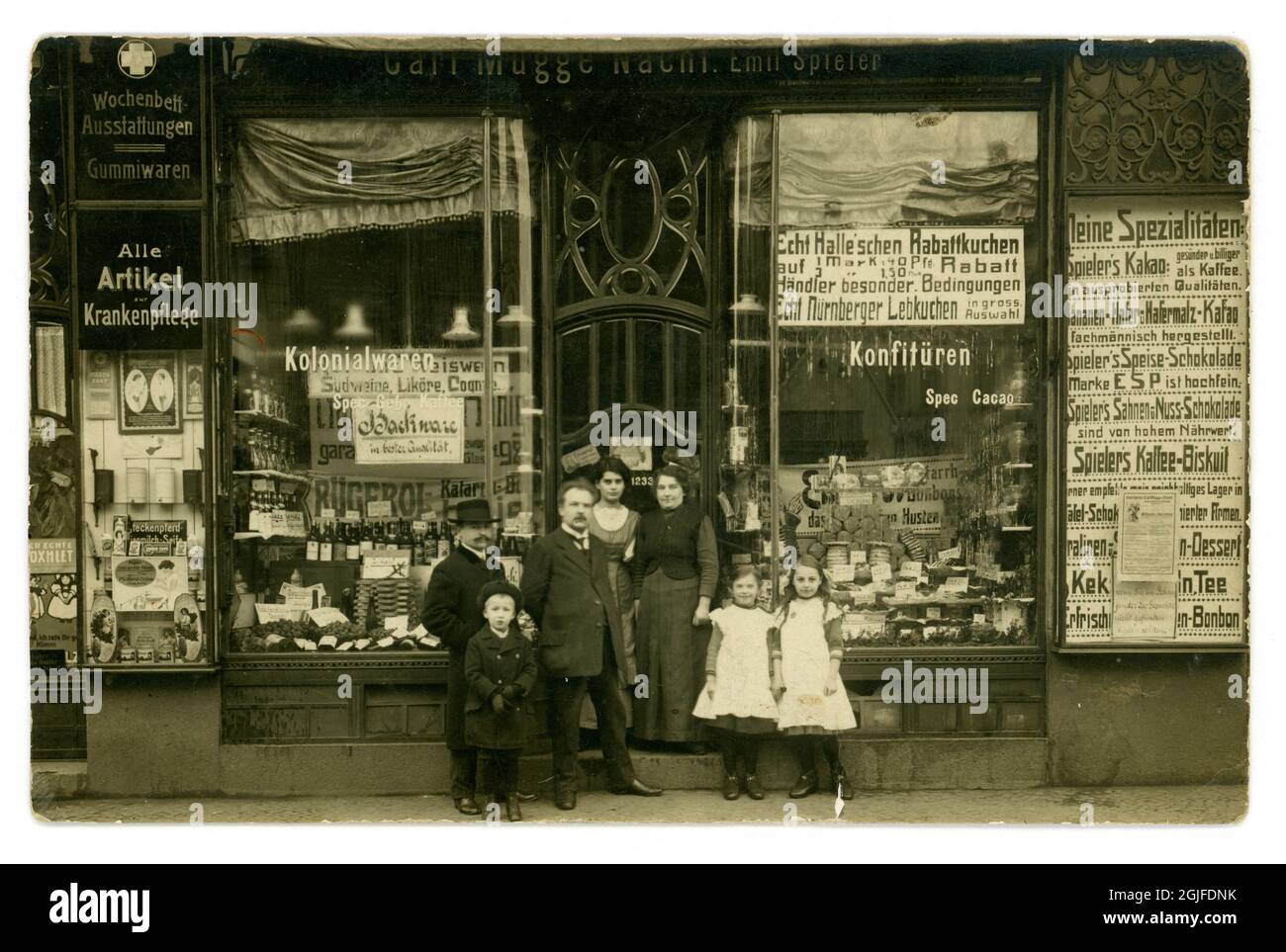 German family and proprietors outside a large grocery shop front, lots of brands, cakes, tea and coffee, special offers posters, well-dressed men, the proprietors perhaps - the  shop sign reads Carl Mugge Nacht Emil Spieler  circa 1914, Germany Stock Photo
