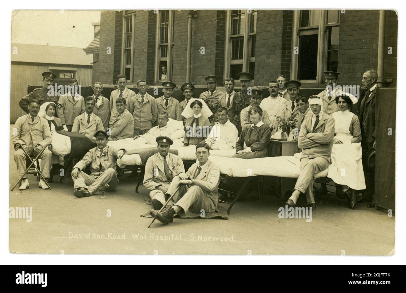 Original WW1 era photographic postcard of wounded soldiers with nurses, (many of them members of the local Voluntary Aid Detachments or VADs) outside Davidson Rd. War Hospital, South Norwood, London, U.K. Even the ward beds have been taken outside. The hospital was in operation from 1915-1919. Stock Photo