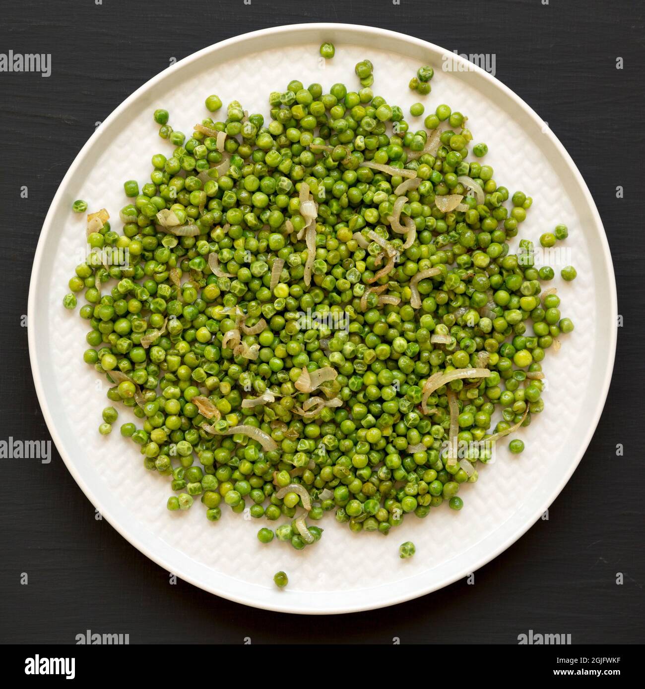 Homemade Sauteed Green Peas on a plate on a black surface, top view