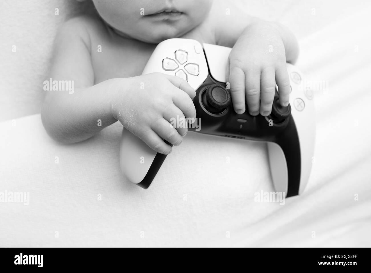 a newborn baby is holding a playstation. fingers of the hands of a newborn. black and white studio photography. Stock Photo