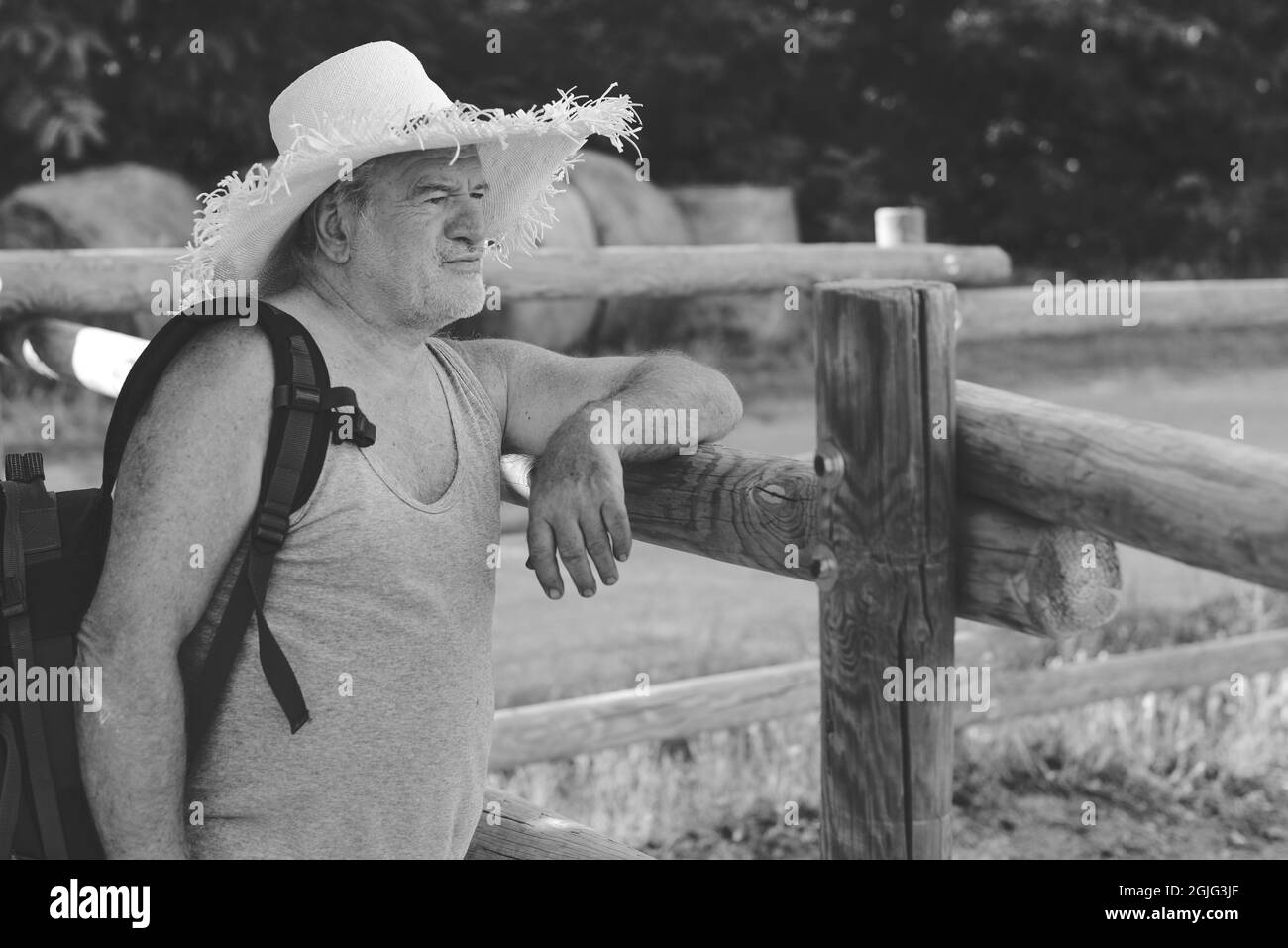 Caucasian senior man wearing a straw hat and standing near a wooden fence on a farm Stock Photo