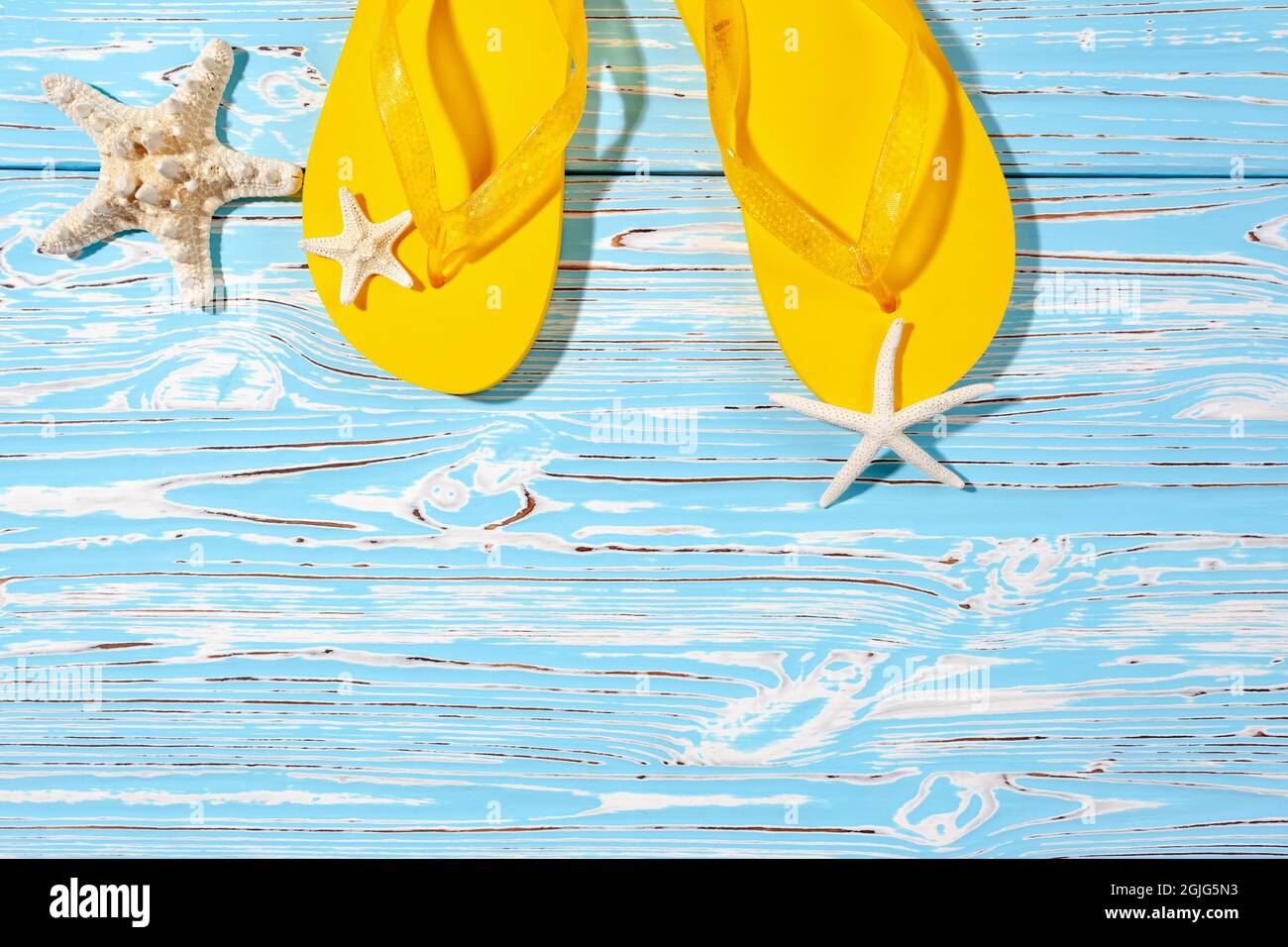 yellow rubber beach flip flops and starfish on a blue wooden background ...