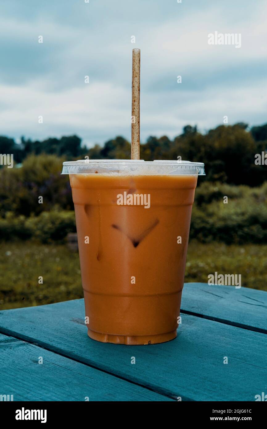Retro stylized plastic cup of iced coffee with milk and sugar and  biodegradable straw on picnic table outside at a park Stock Photo - Alamy