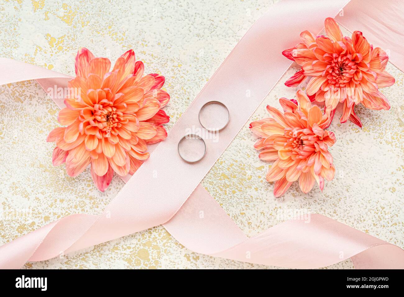 Pair of wedding rings, ribbon and beautiful flowers on color background Stock Photo