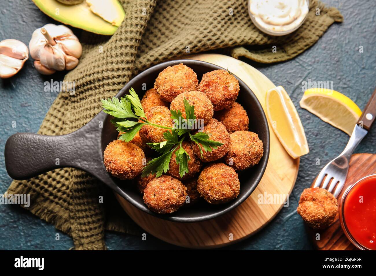 Frying pan with tasty cod cutlets and sauces on dark background Stock Photo