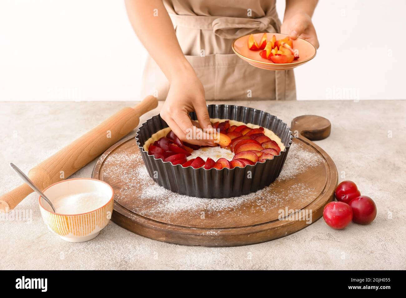 Woman cooking plum pie at table Stock Photo