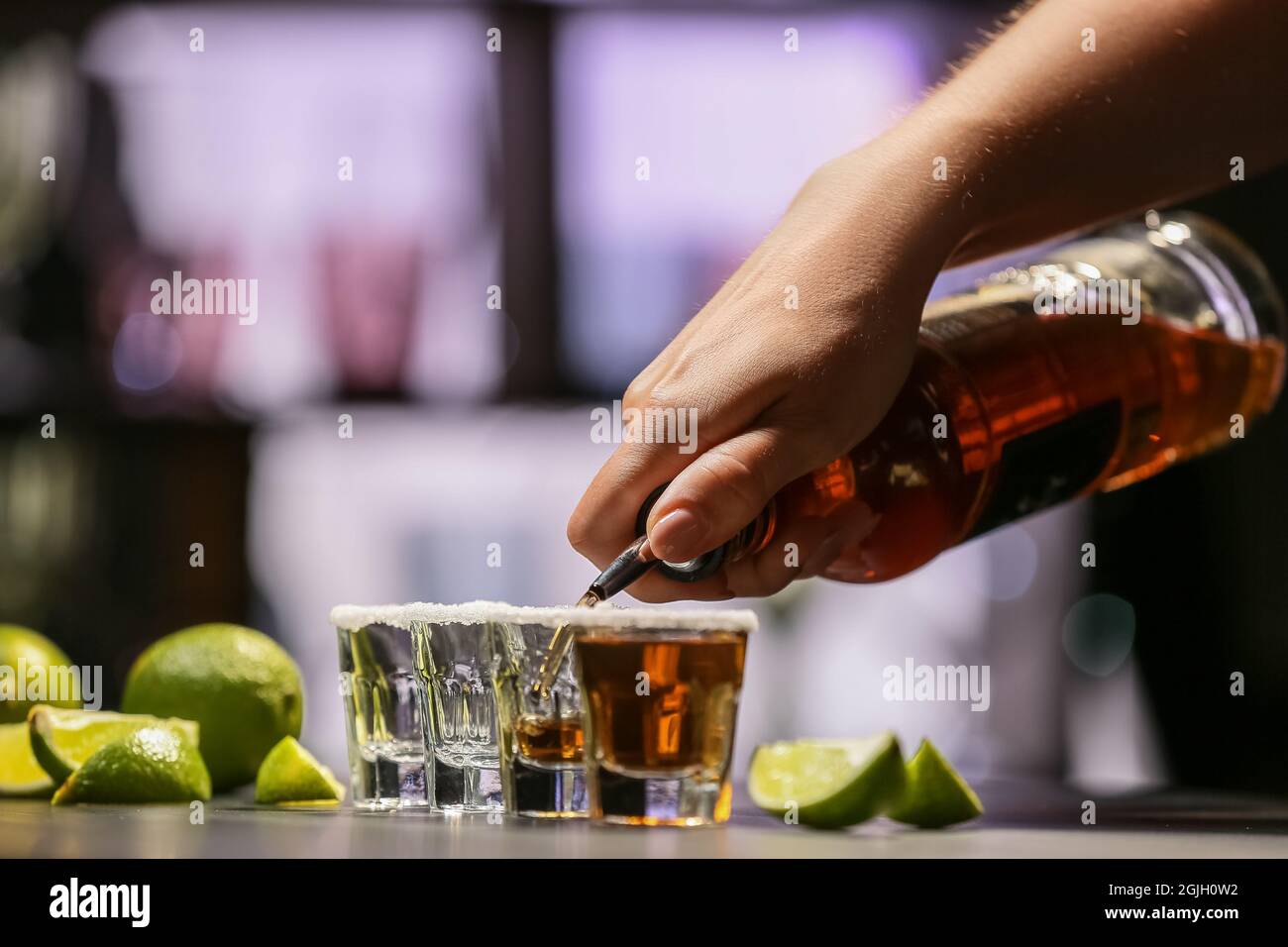 Bartender pouring tasty tequila into glasses at table in bar Stock