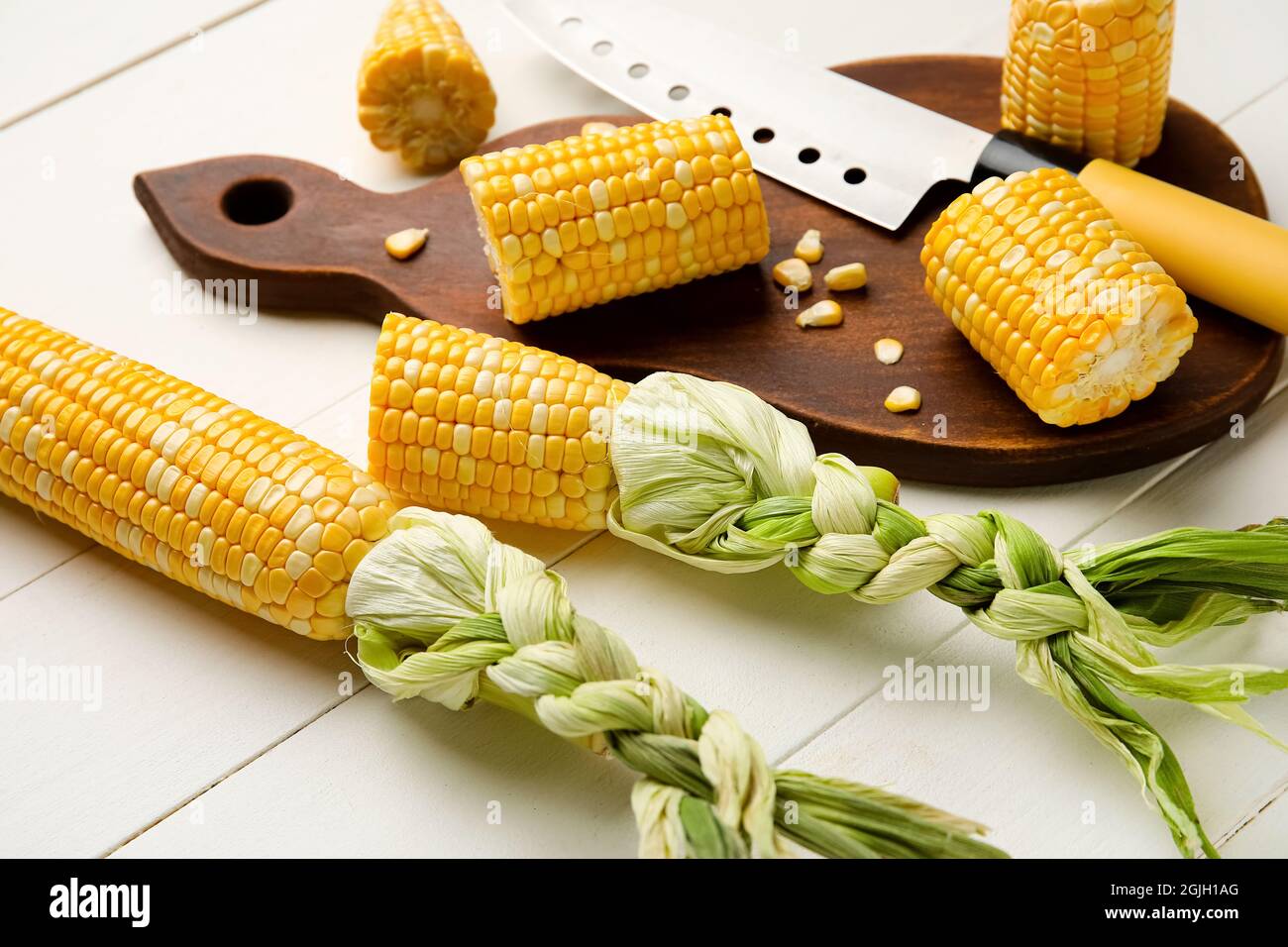 Board with fresh corn cobs and knife on white wooden table Stock Photo ...