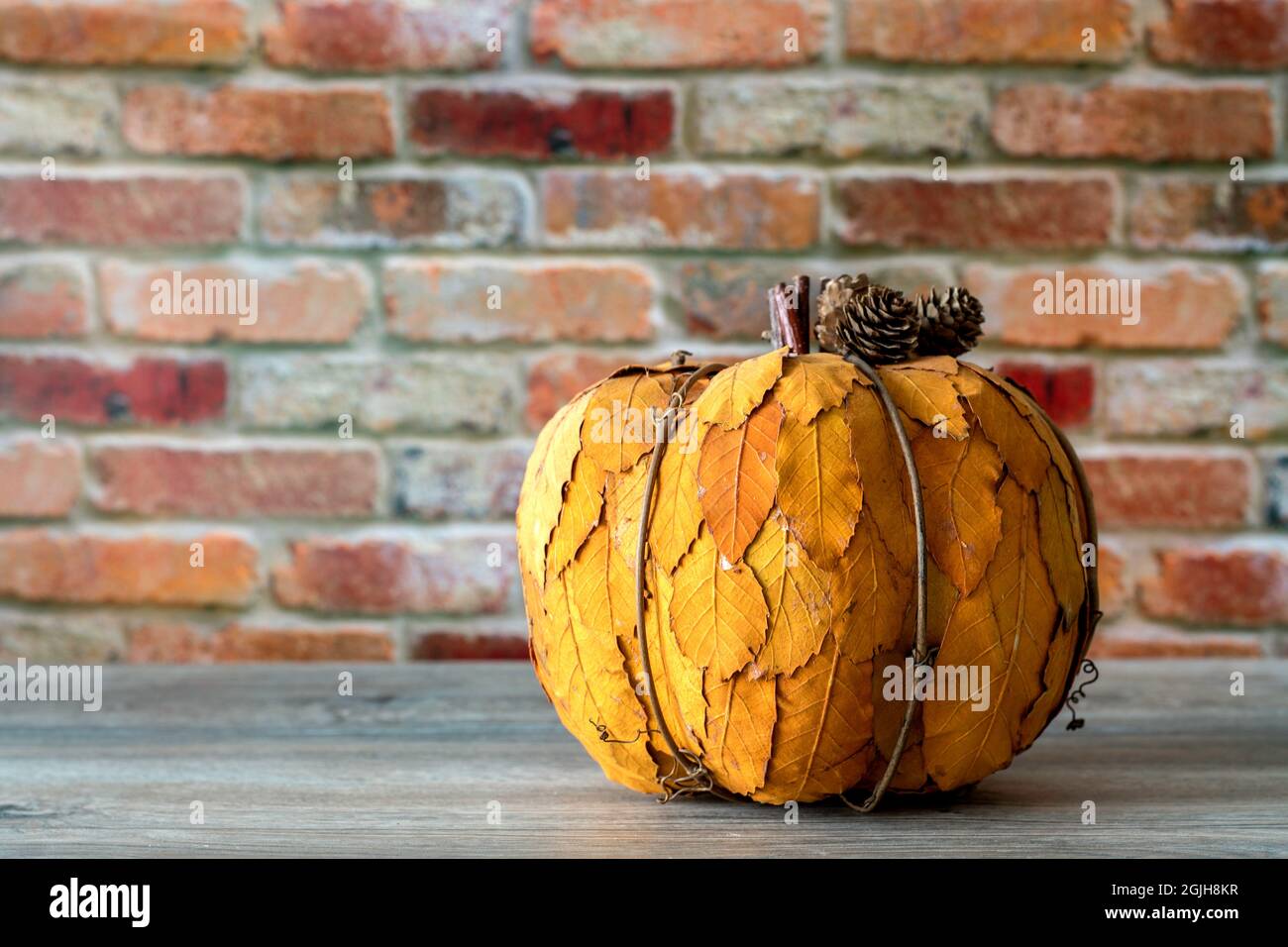 Decorative pumpkin made of yellow leafs isolated against red brick wall background. Thanksgiving concept Stock Photo