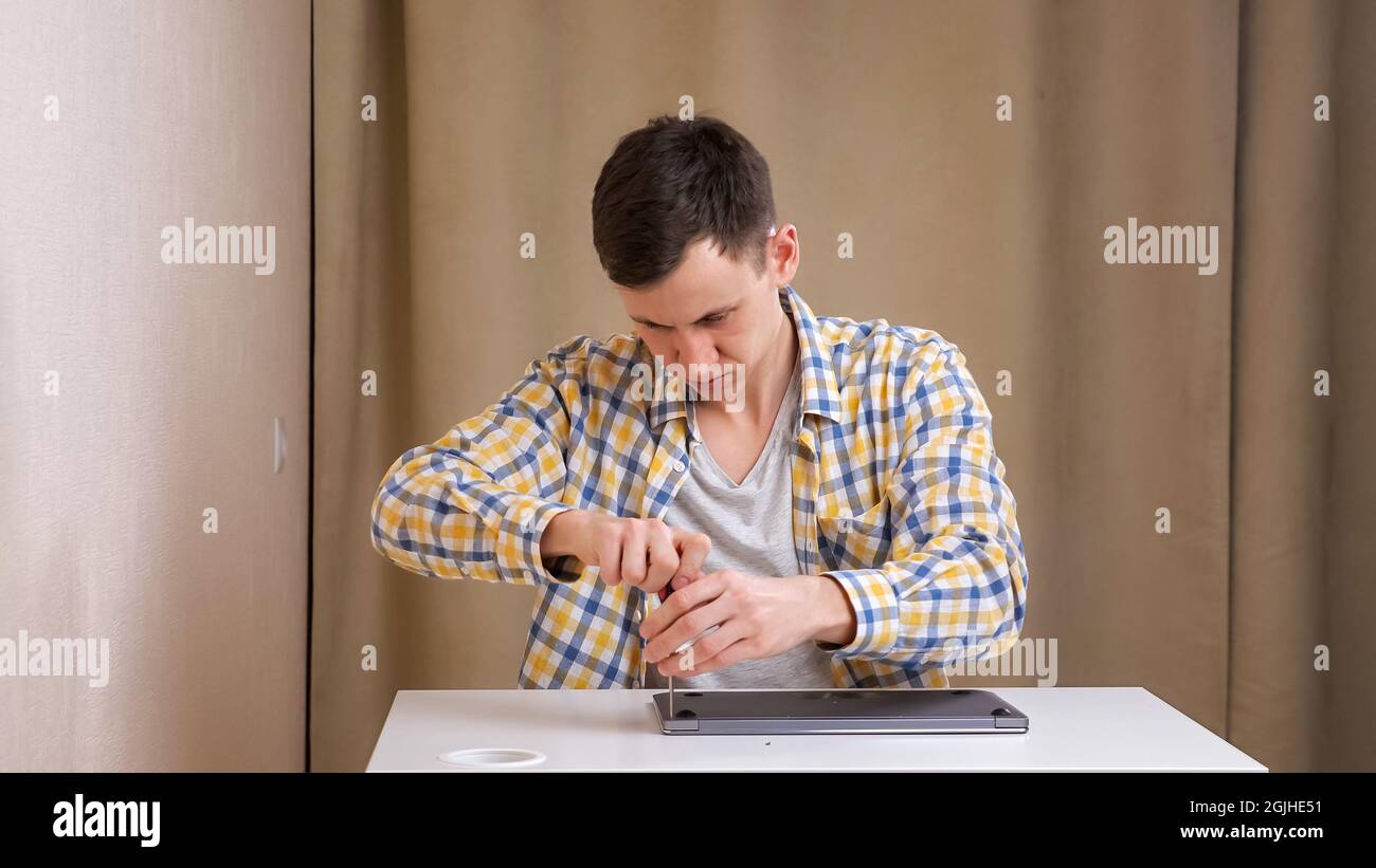 Young man disassembles a laptop with a screwdriver while sitting at table Stock Photo