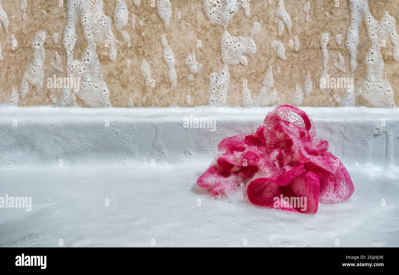 Pink plastic shower loofah covered with bubbles. Stock Photo