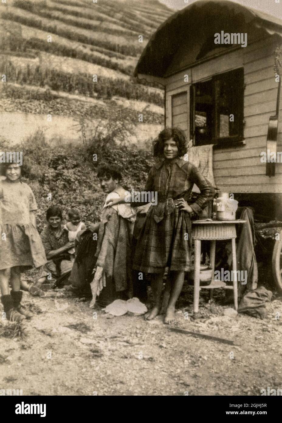A gypsy or Roma family in Germany or France in the late 1920s or early 1930s, beside their traditional wooden caravan and with a hillside cultivated with rows of vines rising behind.  Smiling and apparently carefree before the Second World War and rigorous enforcement of anti-gypsy legislation by the Nazi regime.  Vintage photograph. Stock Photo