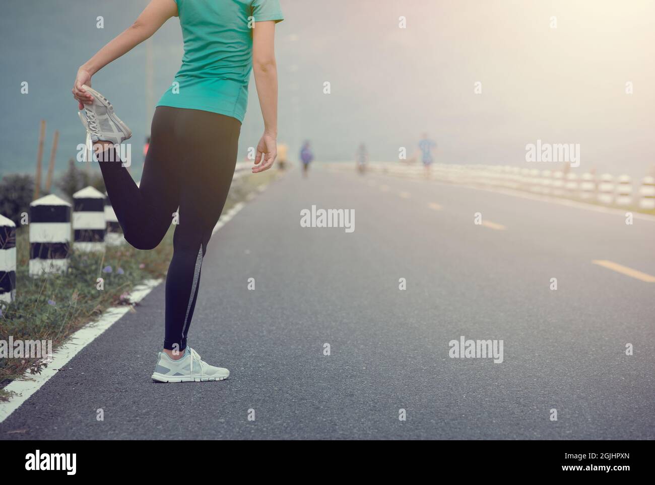 Young woman runner stretching legs before run on  road. Stock Photo