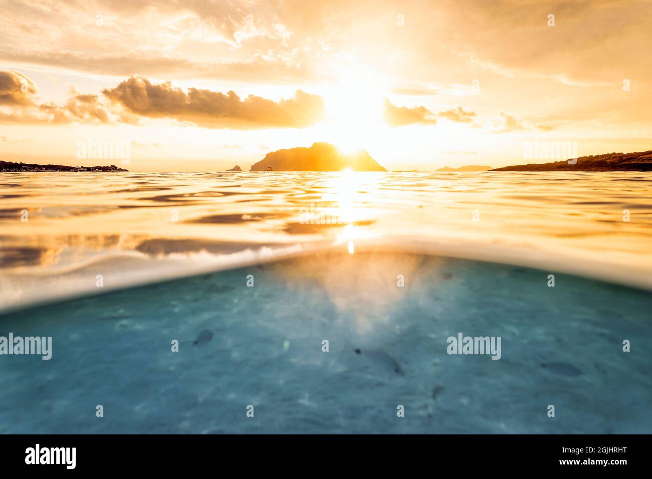 Split shot, over under water surface. Defocused fish under the waterline with Tavolara Island on the surface during a dramatic sunrise. Stock Photo